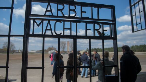 People are seen behind the gate reading Arbeit macht frei (work makes you free) at the entrance to the memorial site of the former Sachsenhausen Nazi concentration camp as they arrive to attend an event to commemorate the 70th anniversary of the camp's liberation, on April 19, 2015 in Oranienburg near Berlin, northeastern Germany. - Sputnik International