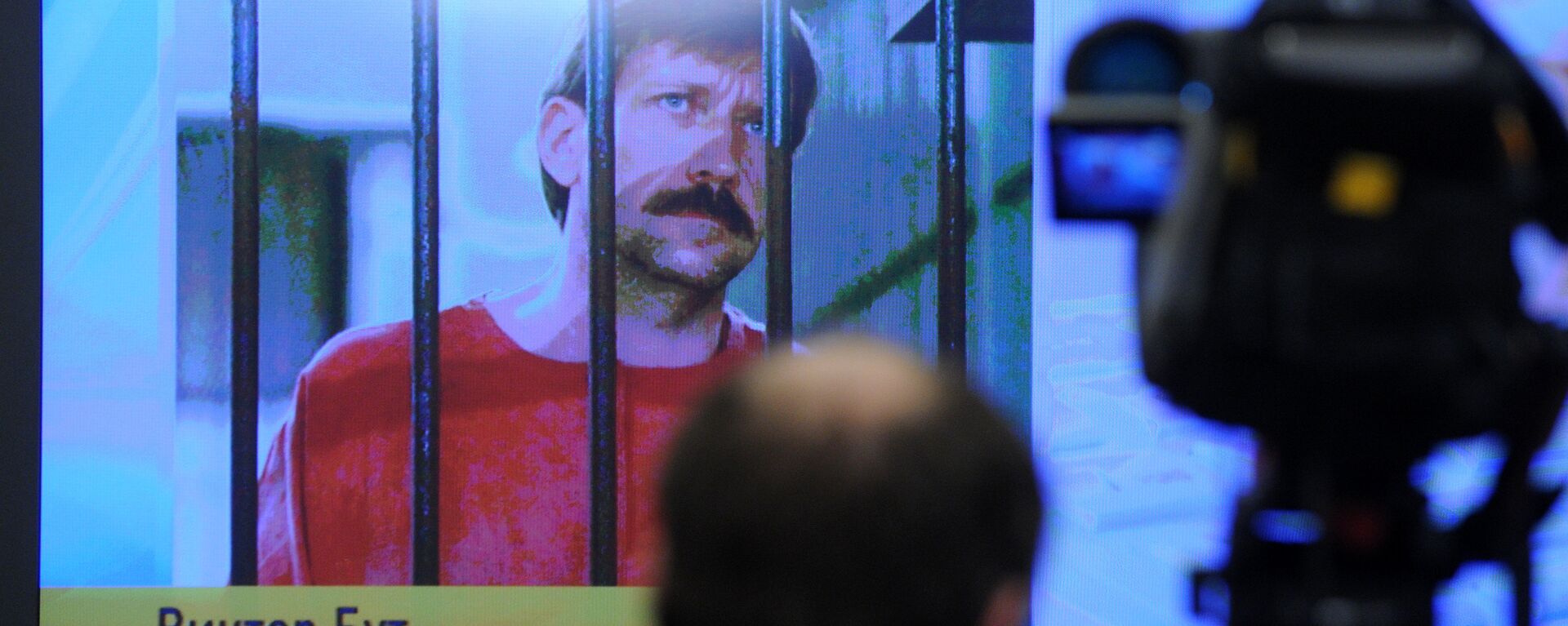 A journalist stands near a screen displaying convicted Russian arms smuggler Viktor Bout in Moscow, on 12 April 2012, during a teleconference with Bout from his US prison - Sputnik International, 1920, 26.10.2020