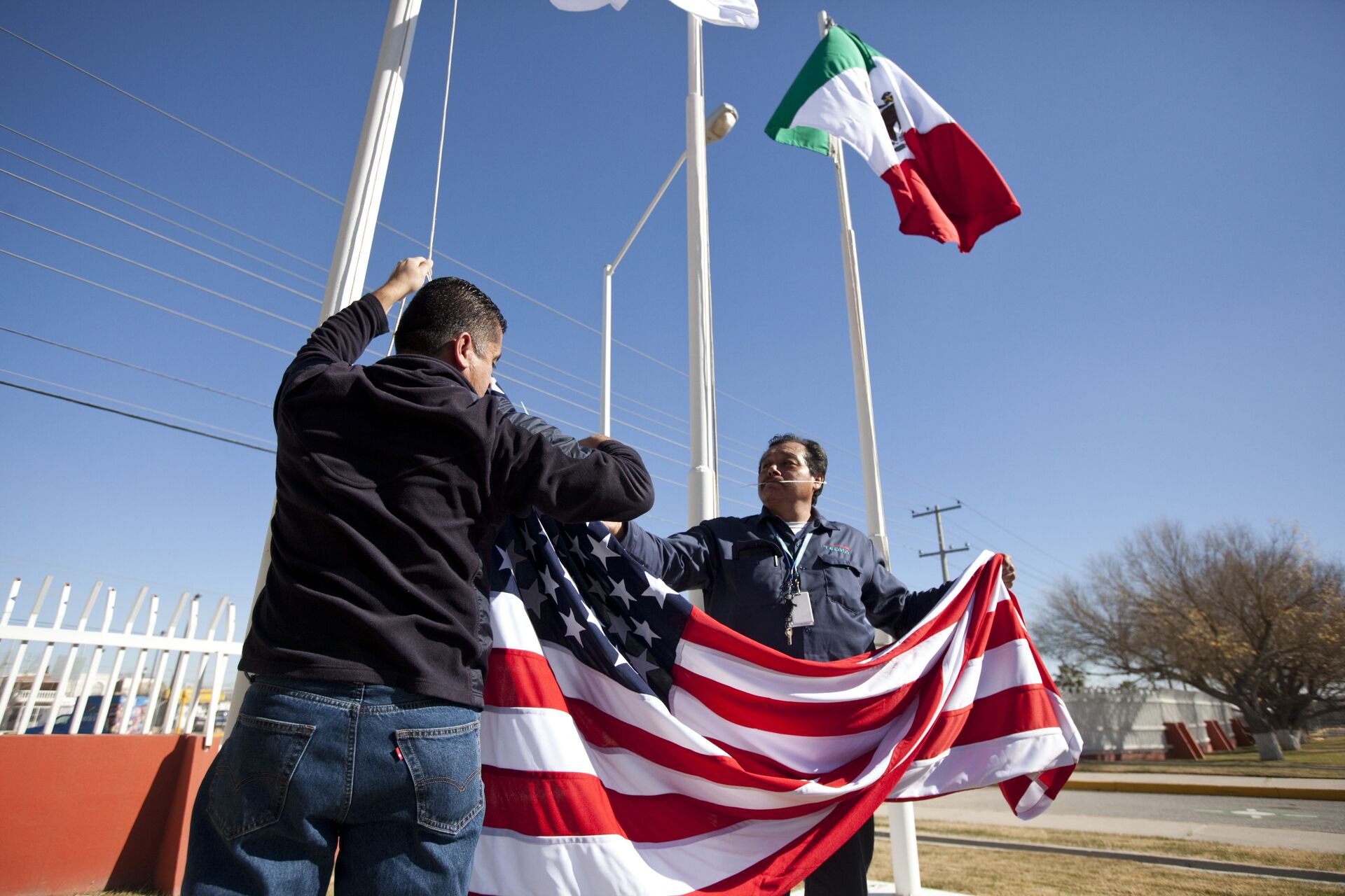 In this Friday, Dec. 27, 2013 photo, workers at one of maquiladoras of the TECMA group prepare to raise the U.S. flag along with the Mexican and TECMA flags in Ciudad Juarez, Mexico - Sputnik International, 1920, 07.06.2022