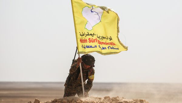 A member of the Syrian Democratic Forces (SDF), made up of US-backed Kurdish and Arab fighters, raises a flag of the SDF near the village of Bir Fawaz, 20 km north of Raqqa, during their offensive towards the Islamic State (IS) group's Syrian stronghold as part of the third phase retake the city and its surroundings, on February 8, 2017 - Sputnik International