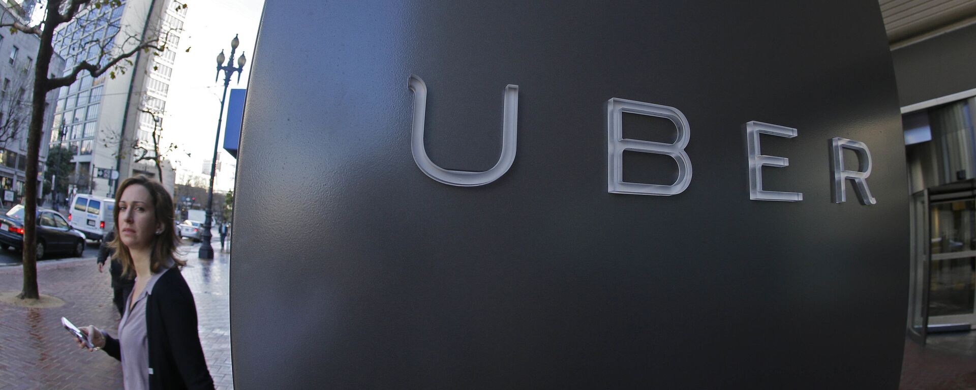 In this file photo taken Tuesday, Dec. 16, 2014, a woman walks past the company logo of the internet car service, Uber, in San Francisco, USA.  - Sputnik International, 1920, 08.12.2020