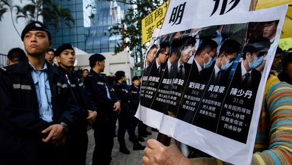 Police (L) stand guard as pro-democracy supporters (R) chant slogans and hold placards after the arrival of the seven police officers (pictured in placard on right), who were found guilty on February 14 of assaulting activist Ken Tsang during the 2014 pro-democracy protests, outside the District Court in Hong Kong on February 17, 2017 - Sputnik International