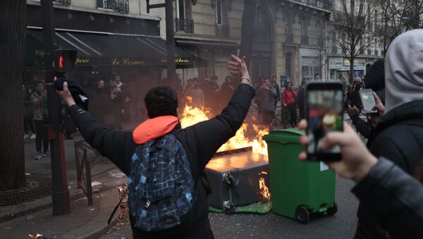 A young man gestures in front of burning dustbins which obstruct the street, during a protest of students against police brutality, following the alleged rape of Theo, next to the Lycee Voltaire secondary school in Paris, on February 23, 2017 - Sputnik International