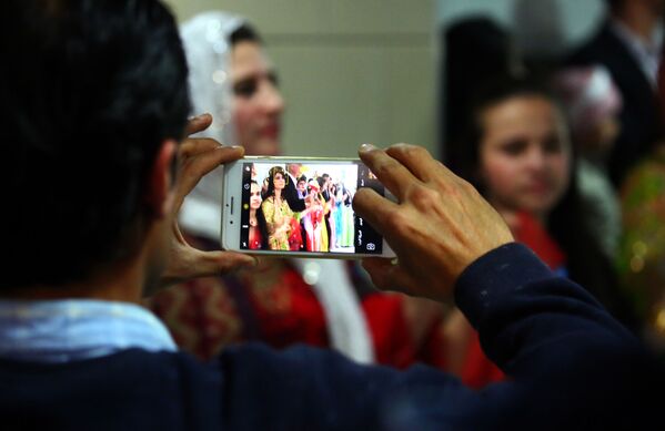 A man takes a photo on his phone of Syrian-Kurdish women modelling traditional Kurdish attire during a fashion show in the northeastern Syrian city of Qamishli on March 10, 2017, which coincides with the Day of Kurdish Clothing. - Sputnik International