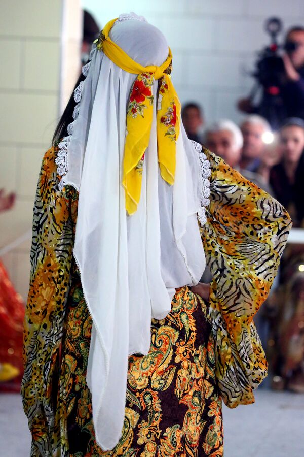 A Syrian-Kurdish female models traditional Kurdish attire consisting of a delicate gown and a white long headscarf with a yellow ribbon on top. - Sputnik International
