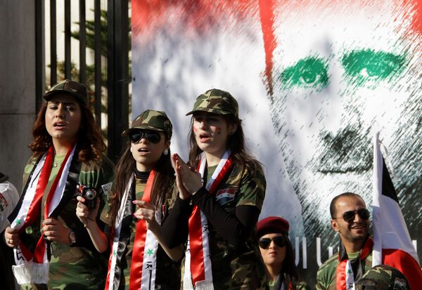 Syrian pro-regime supporters dressed in military uniform stand in front of a mural of President Bashar al-Assad during a rally in Damascus. File photo  - Sputnik International
