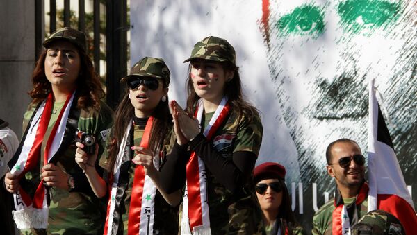 Syrian pro-regime supporters dressed in military uniform stand in front of a mural of President Bashar al-Assad during a rally in Damascus. File photo - Sputnik International