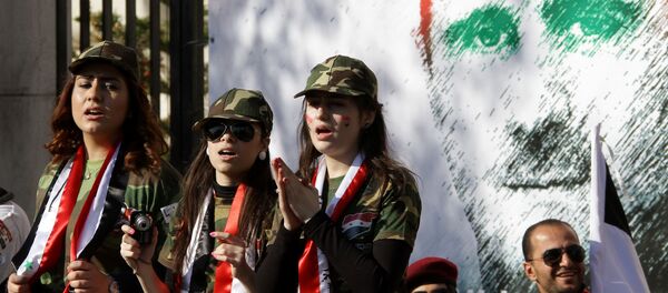 Syrian pro-regime supporters dressed in military uniform stand in front of a mural of President Bashar al-Assad during a rally in Damascus. File photo - Sputnik International
