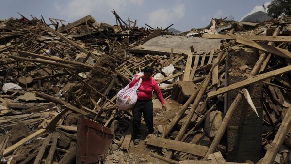 A woman carries her salvaged goods through the rubble of destroyed houses following a massive earthquake in the town of Longtoushan in Ludian County in southwest China's Yunnan Province (File) - Sputnik International