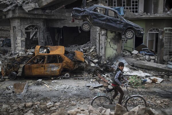 A boy rides his bike past destroyed cars and houses in a neighborhood recently liberated by Iraqi security forces, on the western side of Mosul, Iraq, Sunday, March 19, 2017 - Sputnik International