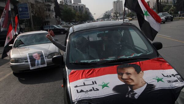 Syrians display national flags and banners with photos of Syrian President Bashar Assad during a pro-government event in Damascus, Syria. (File) - Sputnik International