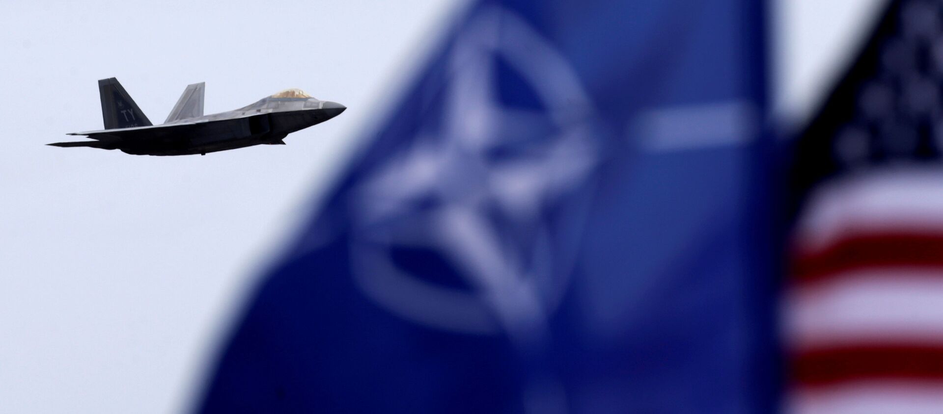NATO and US flags flutter as U.S. Air Force F-22 Raptor fighter flies over the military air base in Siauliai, Lithuania, April 27, 2016. - Sputnik International, 1920, 07.06.2021