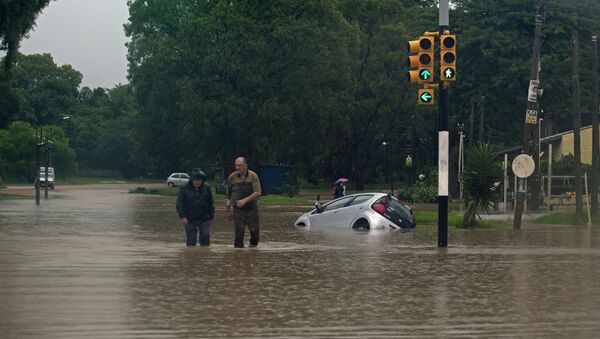 Two men wade through a flooded street in the locality of Solymar, Ciudad de la Costa, Canelones, some 20 km east of Montevideo, during floods caused by heavy rains hitting the country, on February 7, 2014 - Sputnik International