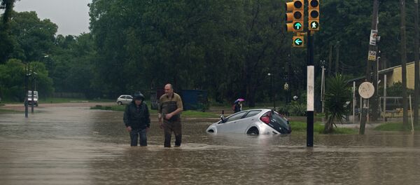 Two men wade through a flooded street in the locality of Solymar, Ciudad de la Costa, Canelones, some 20 km east of Montevideo, during floods caused by heavy rains hitting the country, on February 7, 2014 - Sputnik International