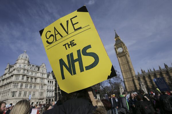 A protester holds a placard in support of the NHS in front of the Elizabeth Tower, also known as Big Ben at the Houses of Parliament during a march against private companies' involvement in the National Health Service (NHS) and social care services provision and against cuts to NHS funding in central London on March 4, 2017 A protester holds a placard in support of the NHS in front of the Elizabeth Tower, also known as Big Ben at the Houses of Parliament during a march against private companies' involvement in the National Health Service (NHS) and social care services provision and against cuts to NHS funding in central London on March 4, 2017 - Sputnik International