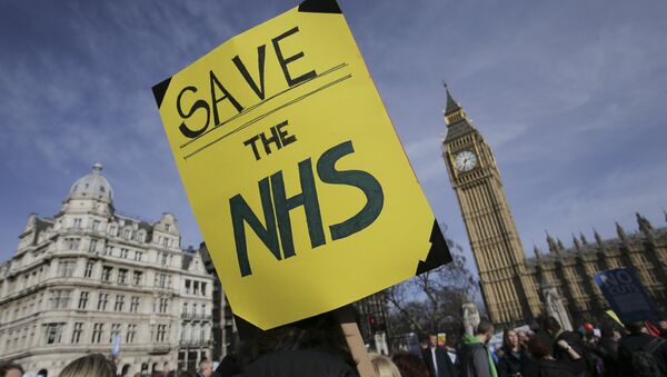 A protester holds a placard in support of the NHS in front of the Elizabeth Tower, also known as Big Ben at the Houses of Parliament during a march against private companies' involvement in the National Health Service (NHS) and social care services provision and against cuts to NHS funding in central London on March 4, 2017 - Sputnik International