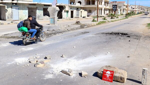 Men ride a motorbike past a hazard sign at a site hit by an airstrike on Tuesday in the town of Khan Sheikhoun in rebel-held Idlib, Syria April 5, 2017 - Sputnik International