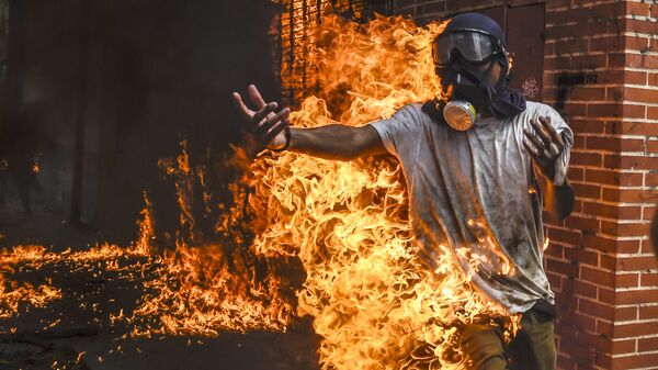 Демонстрант, охваченный огнем от взрыва бензобака мотоцикла, во время протестов в Венесуэле - Sputnik International