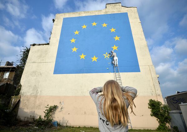 A young girl looks at artwork attributed to street artist Banksy, depicting a workman chipping away at one of the 12 stars on the European Union, seen on a wall in the ferry port of Dover, Britain, May 7, 2017. A young girl looks at artwork attributed to street artist Banksy, depicting a workman chipping away at one of the 12 stars on the European Union, seen on a wall in the ferry port of Dover, Britain, May 7, 2017. - Sputnik International