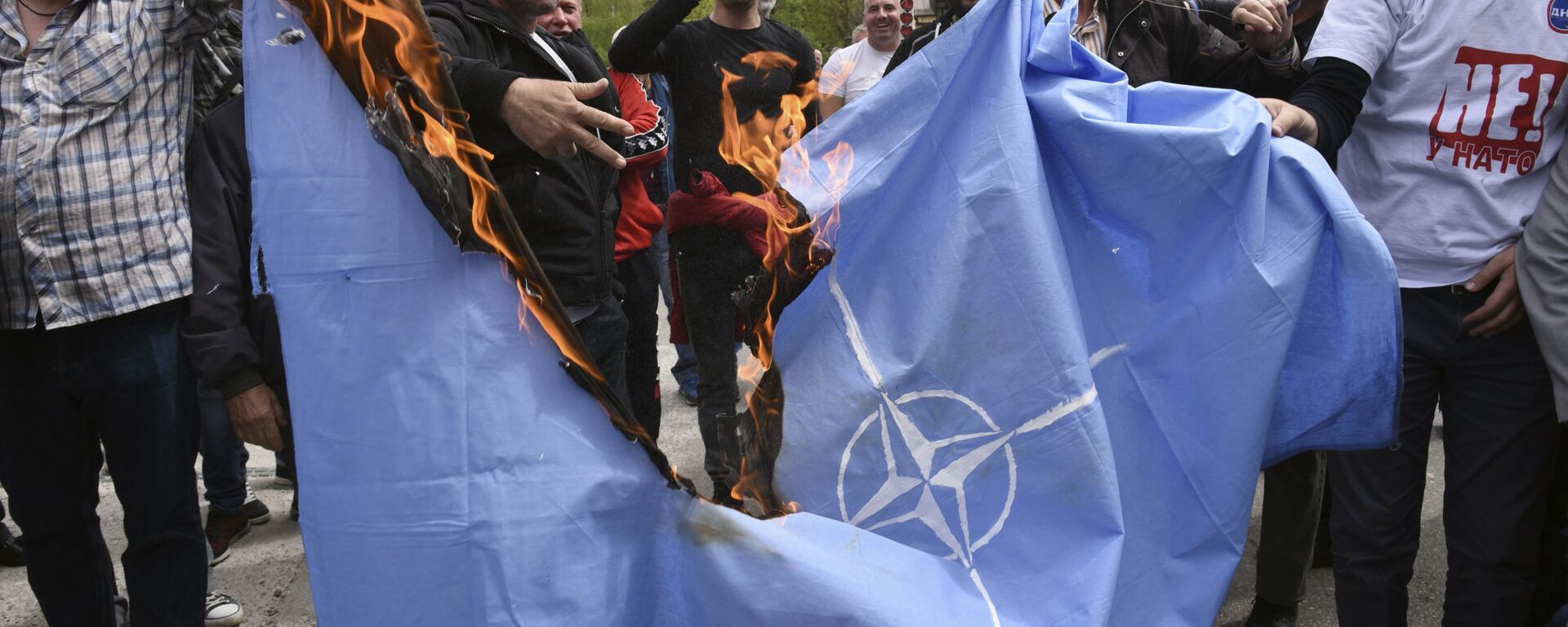 Anti-NATO demonstrators burn a NATO flag in front of a a banner that reads: No to NATO, your hands are bloody - Death to fascism, freedom to the people, during a protest outside the hall before the parliament session in Cetinje, Montenegro, Friday, April 28, 2017 - Sputnik International, 1920, 04.06.2017