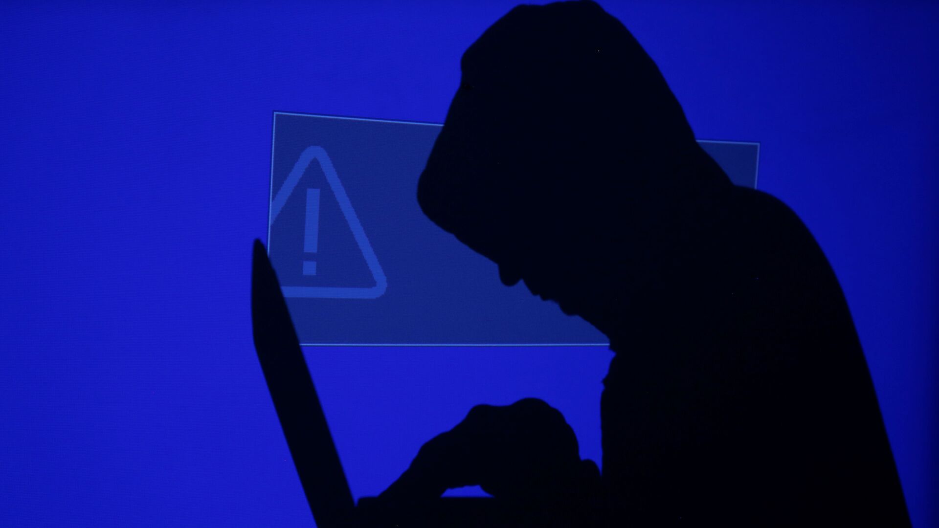 A hooded man holds a laptop computer as blue screen with an exclamation mark is projected on him in this illustration picture taken on May 13, 2017 - Sputnik International, 1920, 08.11.2021