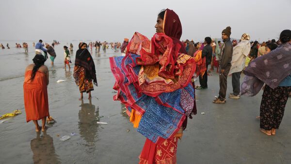 A woman holds saris of companions taking holy dips at the confluence of the Bay of Bengal and Ganges River on Makar Sankranti festival in Gangasagar, India, Saturday, Jan. 14, 2017 - Sputnik International
