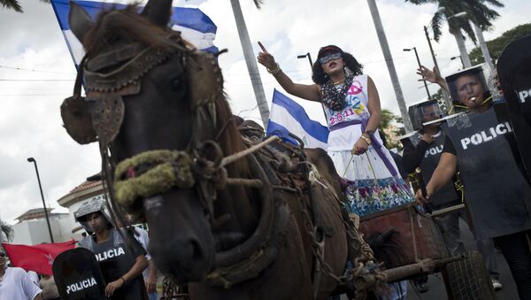 An anti-government protester dressed in the likeness of Nicaragua's first lady Rosario Murillo, navigates a chariot accompanied by a protective cordon of fellow protesters dressed as riot police, in a performance during a demonstration near the Supreme Electoral Council, where anti-government protesters gather every Wednesday demanding fair elections in 2016, in Managua, Nicaragua, Wednesday, Aug. 26, 2015 - Sputnik International