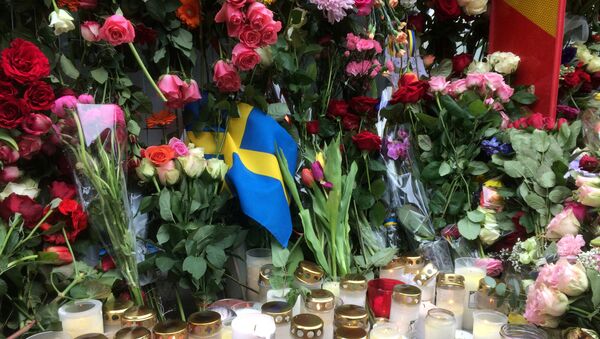Sweden's flag is seen among flowers near the crime scene in central Stockholm April 8, 2017, the day after a hijacked beer truck plowed into pedestrians on Drottninggatan and crashed into Ahlens department store. - Sputnik International