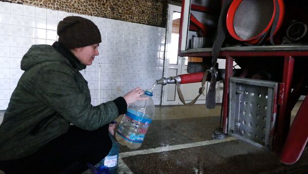 A woman in the Kievsky district of Donetsk gathers process water at the fire station after shelling - Sputnik International