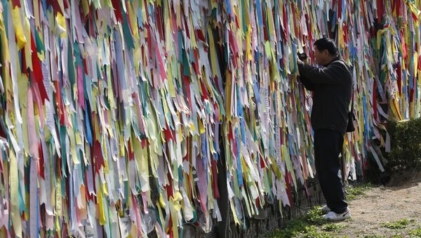 A visitor films through a wire fence decorated with ribbons carrying messages visitors left wishing for the reunification of the two Koreas at the Imjingak Pavilion near the border with North Korea, in Paju, in Seoul, South Korea, Friday, April 15, 2016 - Sputnik International