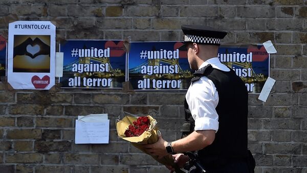 A police officer carries flowers to leave alongside of messages near to where a van was driven at muslims in Finsbury Park, North London, Britain, June 19, 2017 - Sputnik International