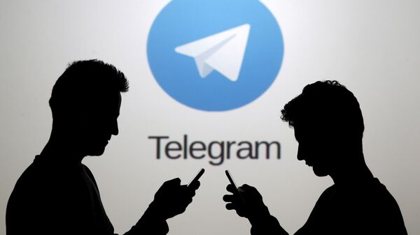 Men pose with smartphones in front of a screen showing the Telegram logo. - Sputnik International