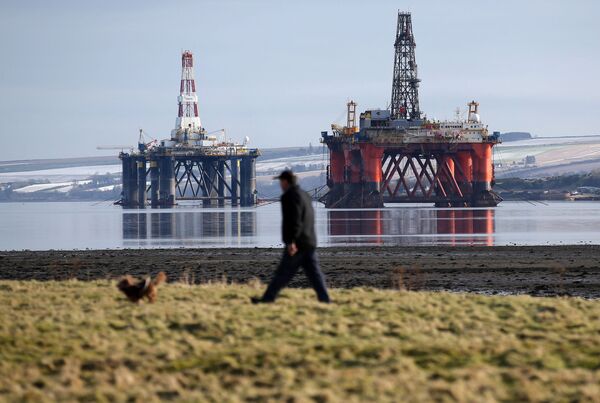 In this Monday Feb. 15, 2016 photo, a man walks past oil platforms laid-up in the Cromarty Firth near Invergordon in the Highlands of Scotland - Sputnik International