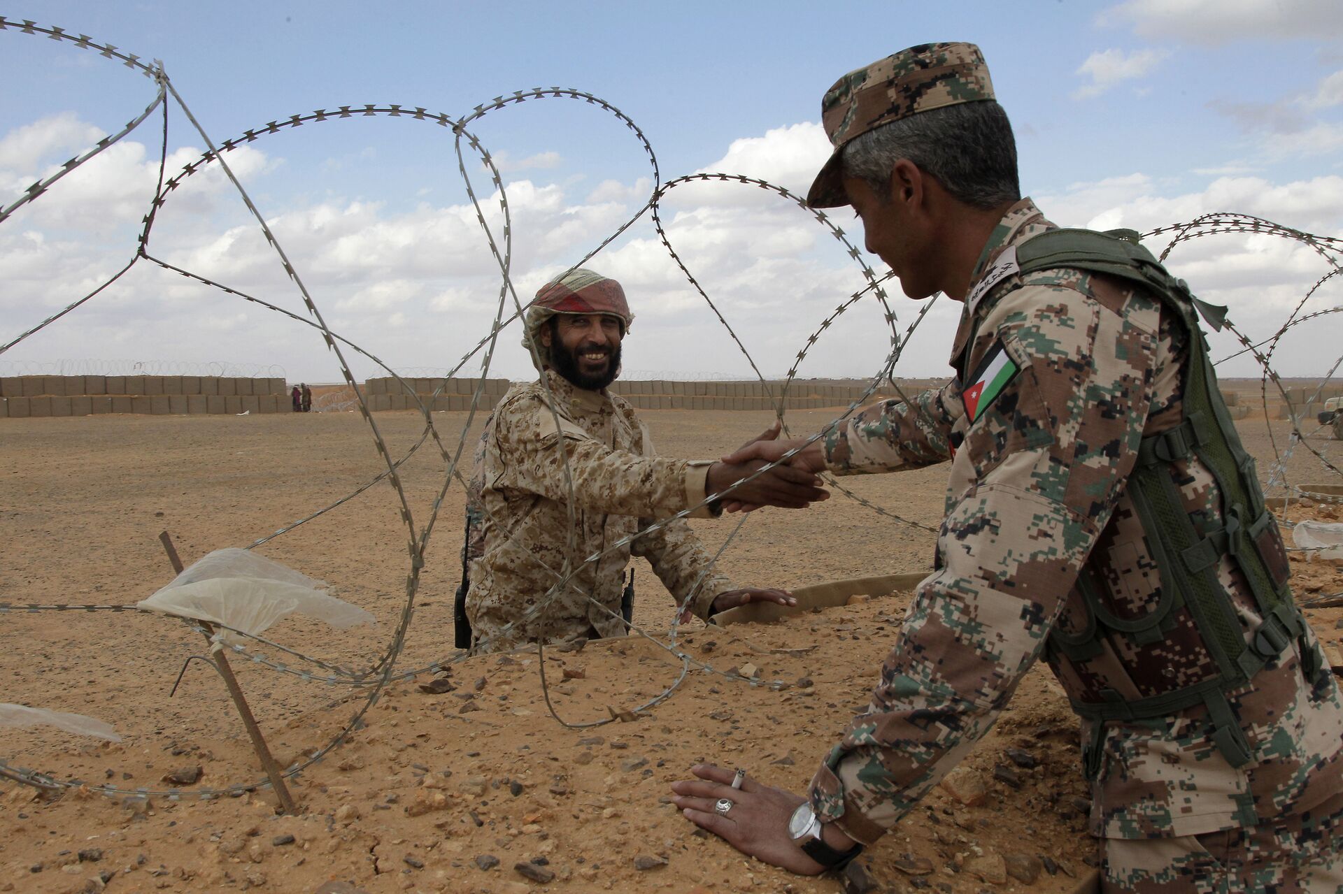 A member of the Syrian Tribes Army, left, that guards the Syrian side of the berm on the north eastern border with Jordan, shakes hands with a Jordanian soldier (File) - Sputnik International, 1920, 20.09.2021