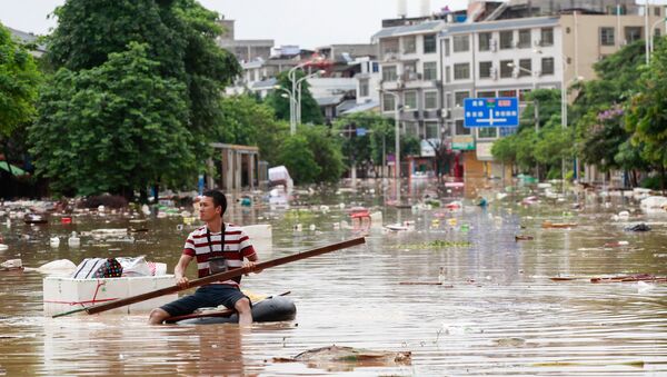 Man using an improvised flotation device to move through floodwaters on a flooded street in Liuzhou, Guangxi province - Sputnik International