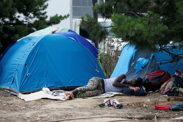 A migrant sleeps next to tents installed in a street near the entrance of the reception center for migrants and refugees at porte de La Chapelle, north of Paris, France, July 6, 2017 A migrant sleeps next to tents installed in a street near the entrance of the reception center for migrants and refugees at porte de La Chapelle, north of Paris, France, July 6, 2017 - Sputnik International