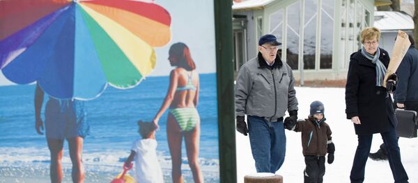 People walk along a snow covered street past an advertisement featuring a pictures of a beach scene in Mariehamn. (File) - Sputnik International