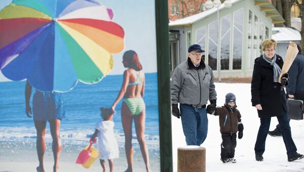 People walk along a snow covered street past an advertisement featuring a pictures of a beach scene in Mariehamn. (File) - Sputnik International