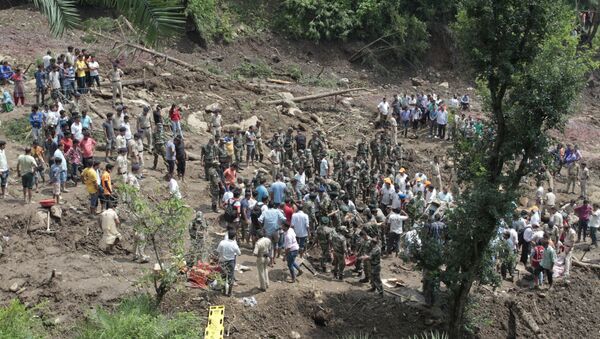 People watch army soldiers and rescue workers recover bodies of landslide victims even as they try to pull out two buses that were covered in mud after a landslide triggered by heavy monsoon rain in Urla village, Himachal Pradesh state, India - Sputnik International