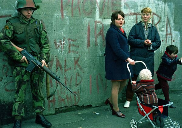 Women and children stand near an armed British military soldier patrols a street in Belfast, Northern Ireland, Feb. 1972. British paratroopers shot 13 demonstrators during a civil rights march on Jan. 30, known as Bloody Sunday. - Sputnik International