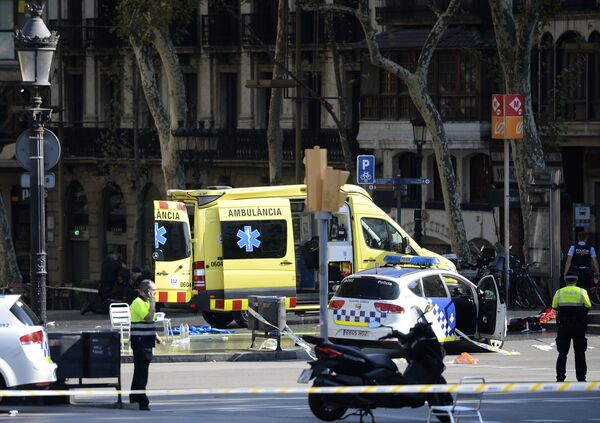 A policemen and a medical staff member stand past police cars and an ambulance in a cordoned off area after a van ploughed into the crowd, injuring several persons on the Rambla in Barcelona on August 17, 2017 - Sputnik International