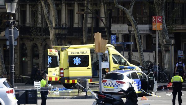 A policemen and a medical staff member stand past police cars and an ambulance in a cordoned off area after a van ploughed into the crowd, injuring several persons on the Rambla in Barcelona on August 17, 2017 - Sputnik International