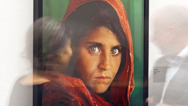 In this picture taken with a long time exposure people walk in front of the photo 'Afghan Girl' (Pakistan, 1984) during the exhibition 'Steve McCurry Retrospective' of US photographer Steve McCurry in the Kunsthalle (Art Hall) in Erfurt, Germany, Wednesday, Feb. 26, 2014.  - Sputnik International