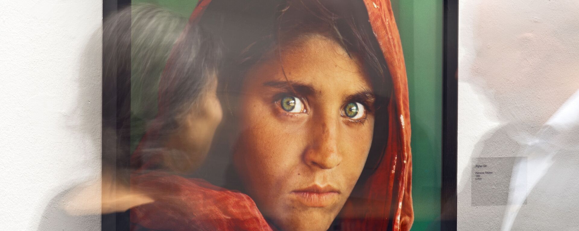 In this picture taken with a long time exposure people walk in front of the photo 'Afghan Girl' (Pakistan, 1984) during the exhibition 'Steve McCurry Retrospective' of US photographer Steve McCurry in the Kunsthalle (Art Hall) in Erfurt, Germany, Wednesday, Feb. 26, 2014.  - Sputnik International, 1920, 16.10.2021