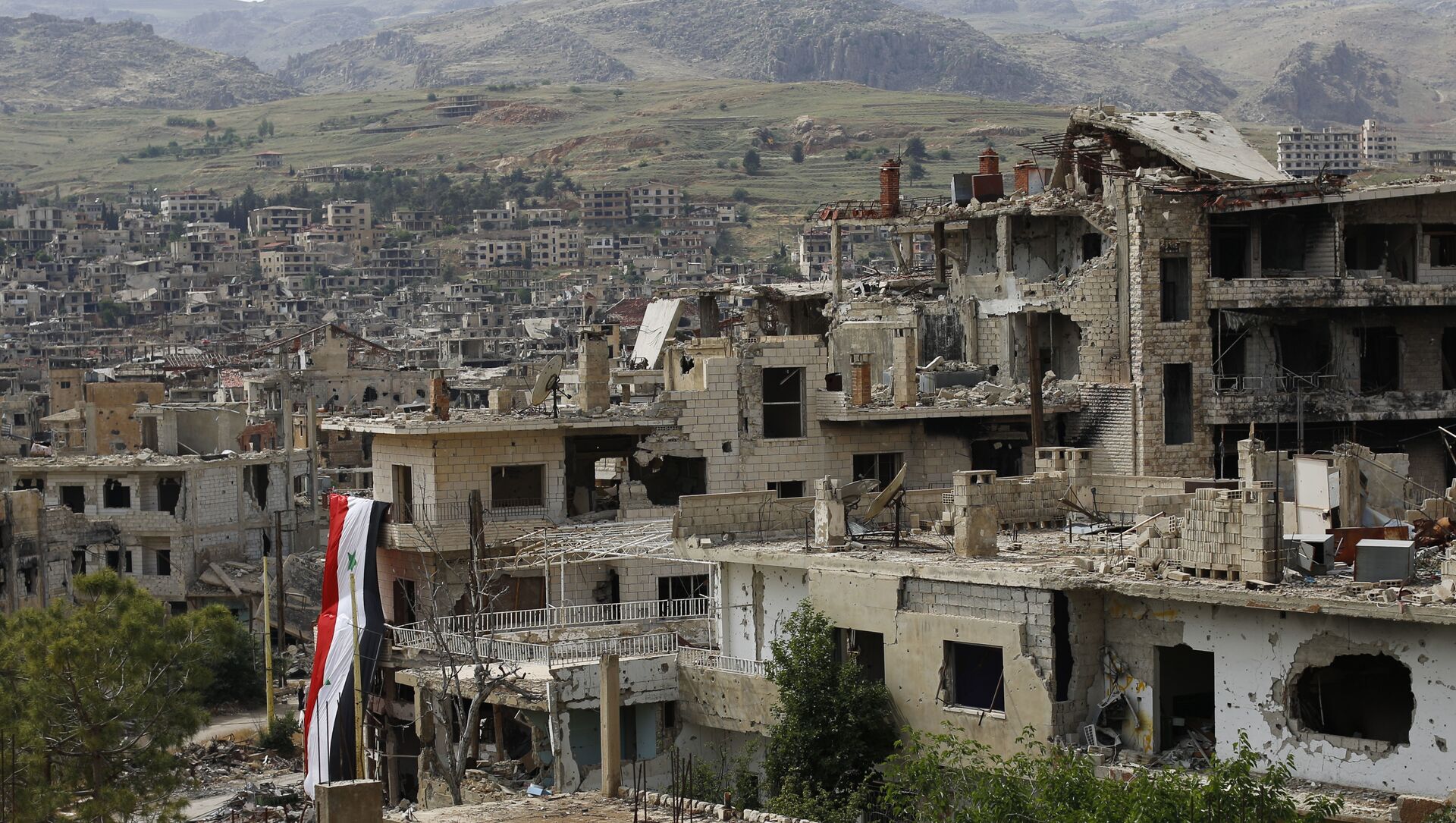 In this May 18, 2017, photo, a Syrian National flag hangs out of a damaged building at the mountain resort town of Zabadani in the Damascus countryside, Syria. - Sputnik International, 1920, 15.03.2021