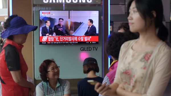 People are seen past a television screen showing a file image of North Korean leader Kim Jong-Un (C) as news anchors (on screen, L and R) provide coverage of this morning's North Korean missile launch, at a railway station in Seoul on August 26, 2017 - Sputnik International