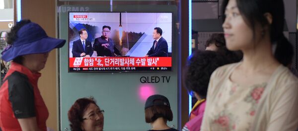 People are seen past a television screen showing a file image of North Korean leader Kim Jong-Un (C) as news anchors (on screen, L and R) provide coverage of this morning's North Korean missile launch, at a railway station in Seoul on August 26, 2017 - Sputnik International
