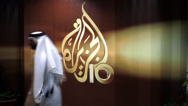 A Qatari employee of Al Jazeera Arabic language TV news channel passes by the logo of Al Jazeera in Doha, Qatar. (File) - Sputnik International