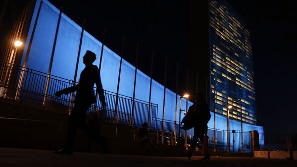 Pedestrians walk by United Nations Headquarters, lit up in blue light, a day in advance of the 70th Anniversary of the U.N., Friday, Oct. 23, 2015, in New York - Sputnik International