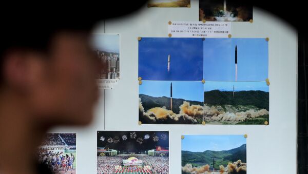 A man drives his car past a display board showing photos of ballistic missile launches in North Korea outside the North Korean Embassy in Beijing - Sputnik International